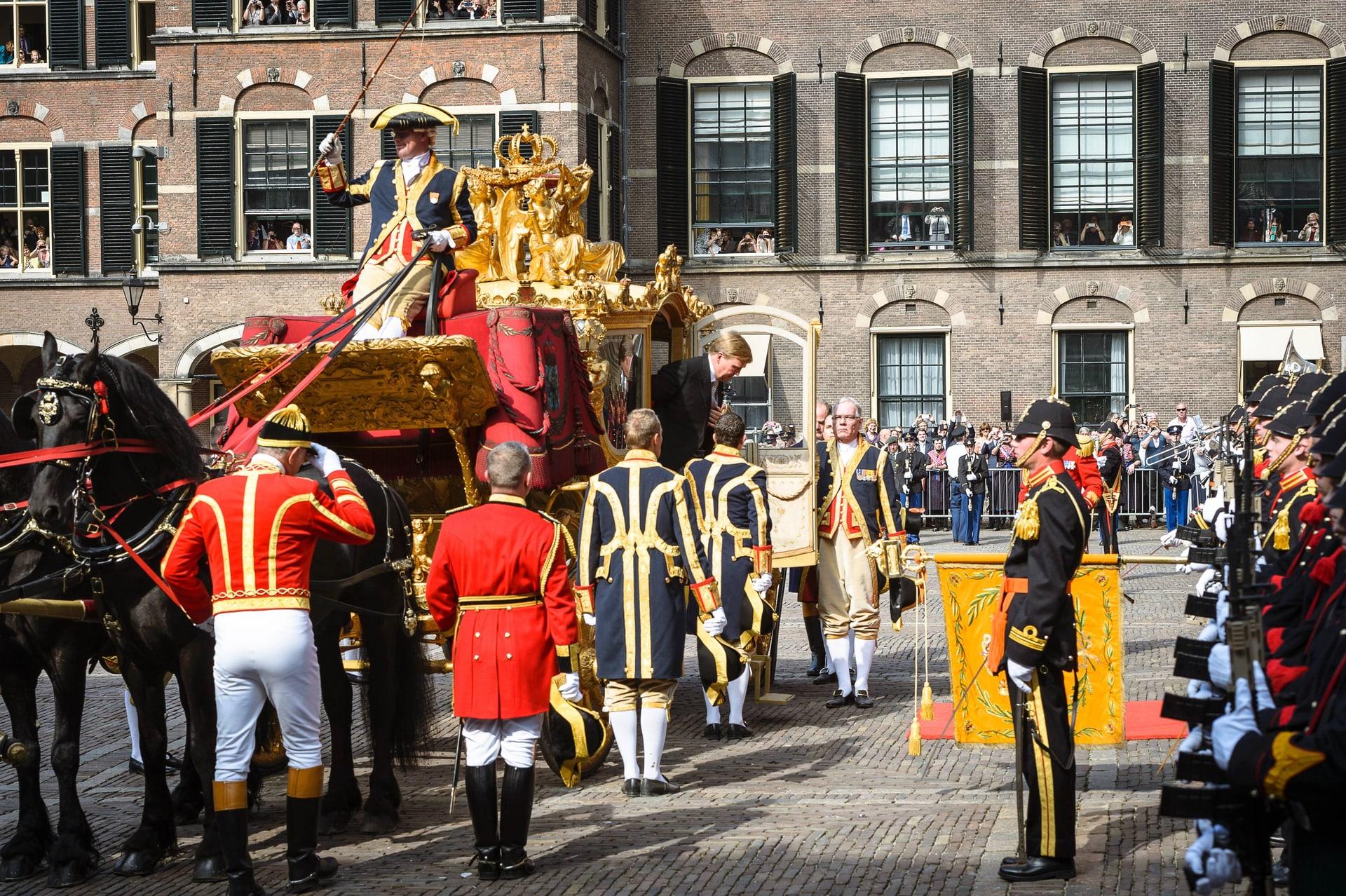 Willem-Alexander stapt op Prinsjesdag 2014 uit de Gouden Koets, omringd door lakeien en militair ceremonieel.